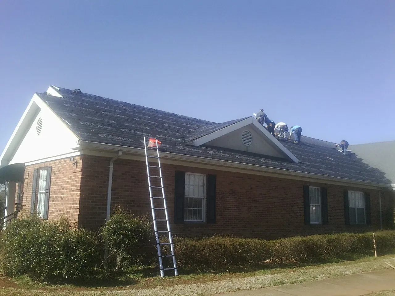 Crew tearing shingles off a brick ranch roof with a ladder set — Emergency Roof Repair work by our crew in York Harbor