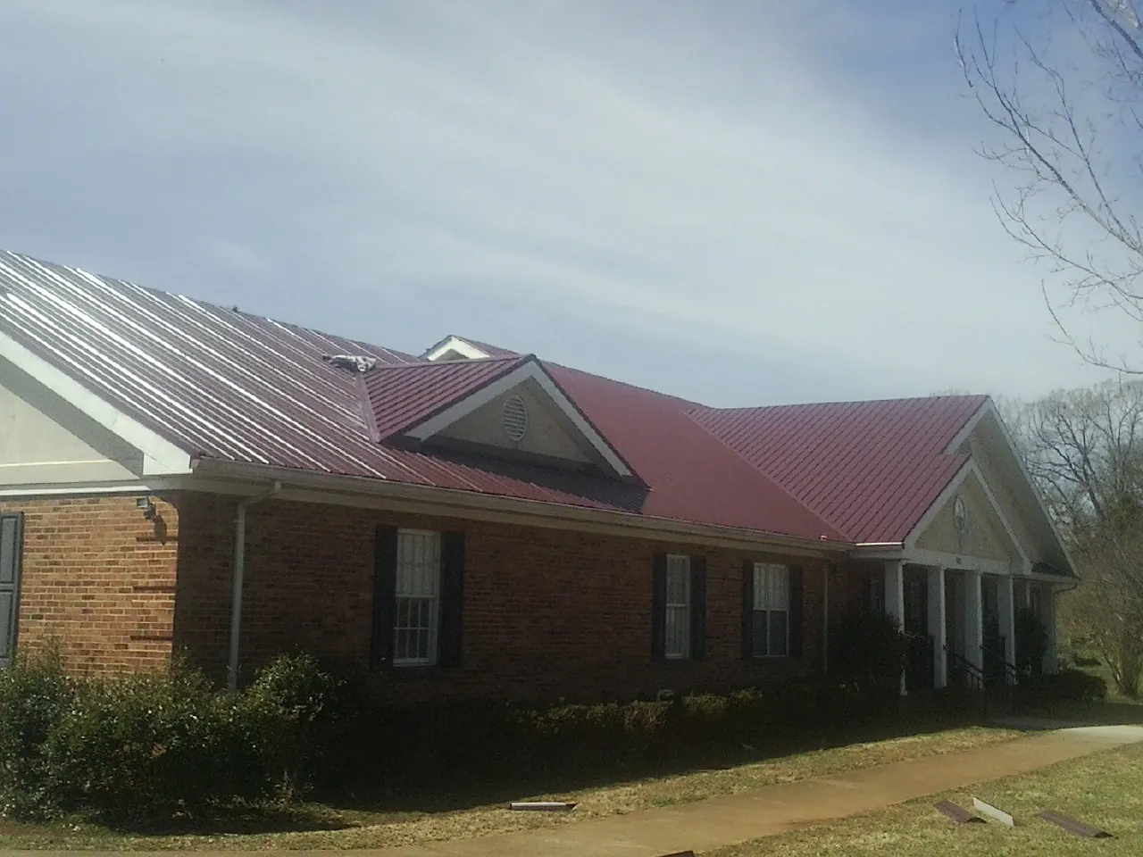 Red metal roof with gabled entries on a long brick building, from a Hail Damage Roof Repair job in York Harbor