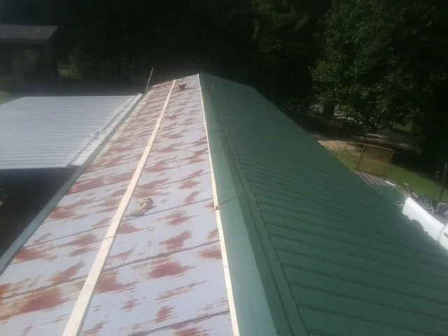 Old rusted panels beside newly installed green metal roofing — Wind Damage Roof Repair by Roofing Brothers in York Harbor