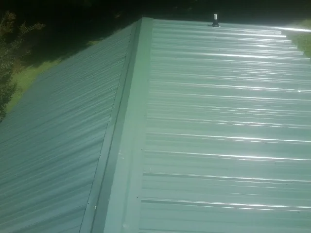 New green metal panels meeting at the ridge of a roof — Flat Roof Repair work by our crew in York Harbor