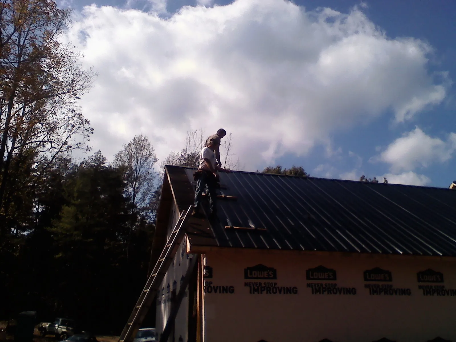 Roofer fastening dark metal panels high against a cloudy sky, from a Roof Inspection job in York Harbor
