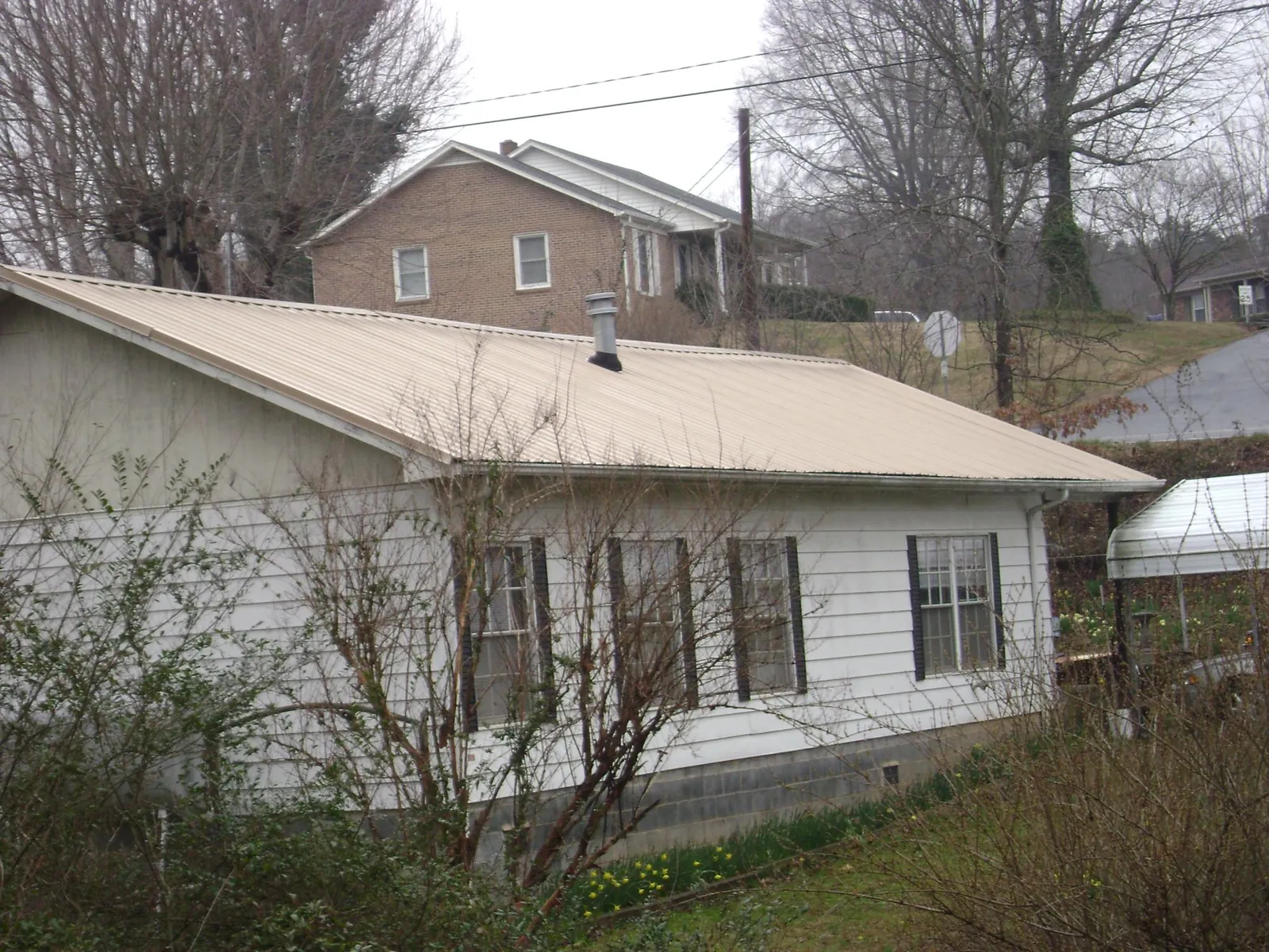 Tan metal roof on a white sided house set into a hillside — Commercial Roofing by Roofing Brothers in York Harbor